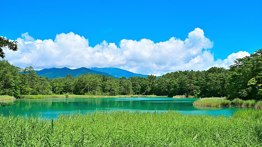 Veduta del lago Bentennuma con acque turchesi circondate da boschi verdi e montagne sotto un cielo blu con nubi.