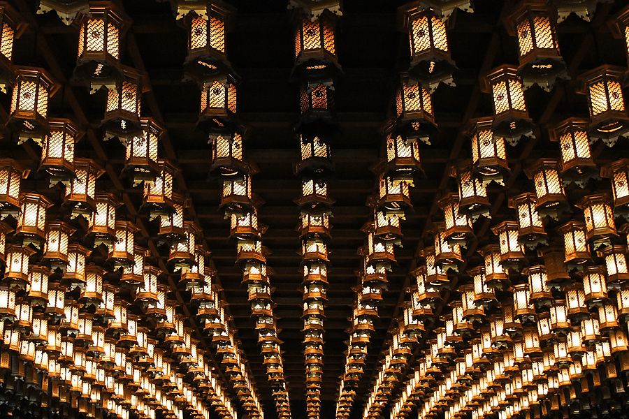 File di lanterne illuminate appese al soffitto in legno scuro all'interno del tempio Daisho-in a Miyajima.