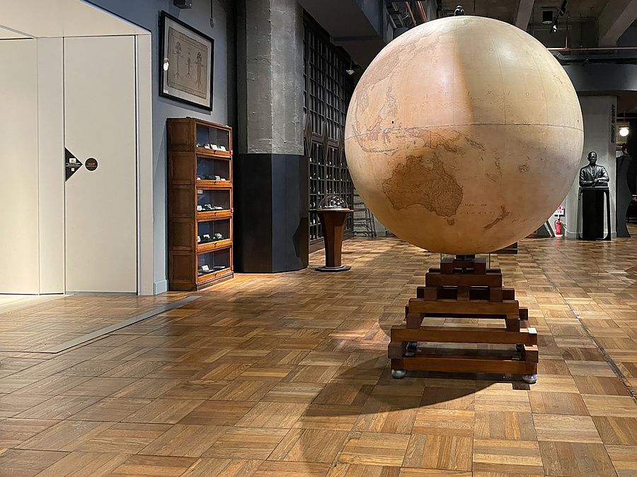 Un grande mappamondo vintage al centro di una sala museale, con pavimento in legno e vetrine espositive.