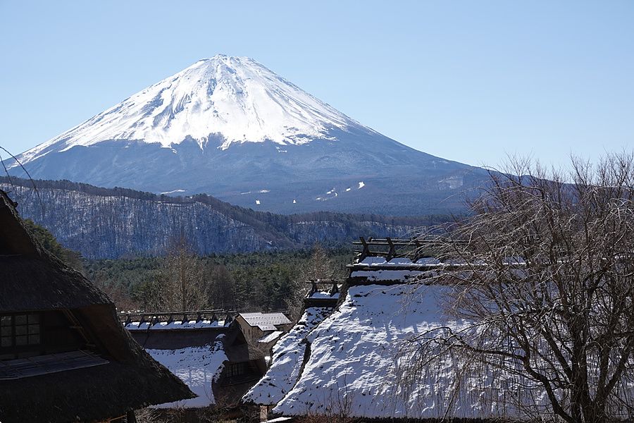 Il monte Fuji innevato si staglia dietro le case tradizionali in legno con tetti di paglia in Giappone.