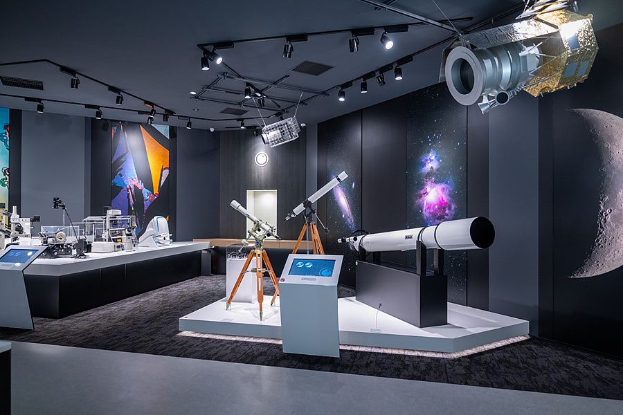 Telescopi e modelli di satelliti in una sala museale moderna con pareti scure e pannelli dedicati al cosmo.