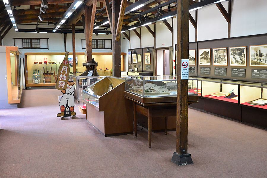 Interno del museo della birreria Gekkeikan a Kyoto con teche, esposizioni storiche e una sagoma pubblicitaria.