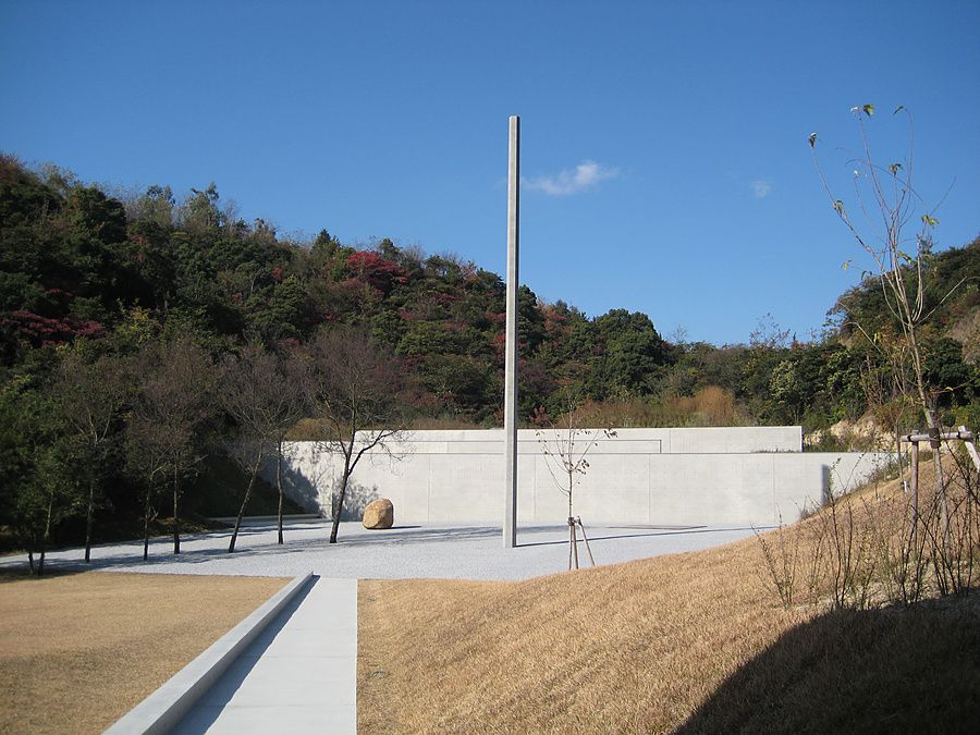 Veduta del Lee Ufan Museum a Naoshima con il suo cortile in ghiaia, il monolite di cemento e il bosco sullo sfondo.