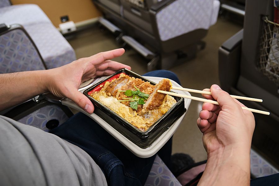 Persona che mangia un bento di katsudon con le bacchette su un sedile di un treno in Giappone.
