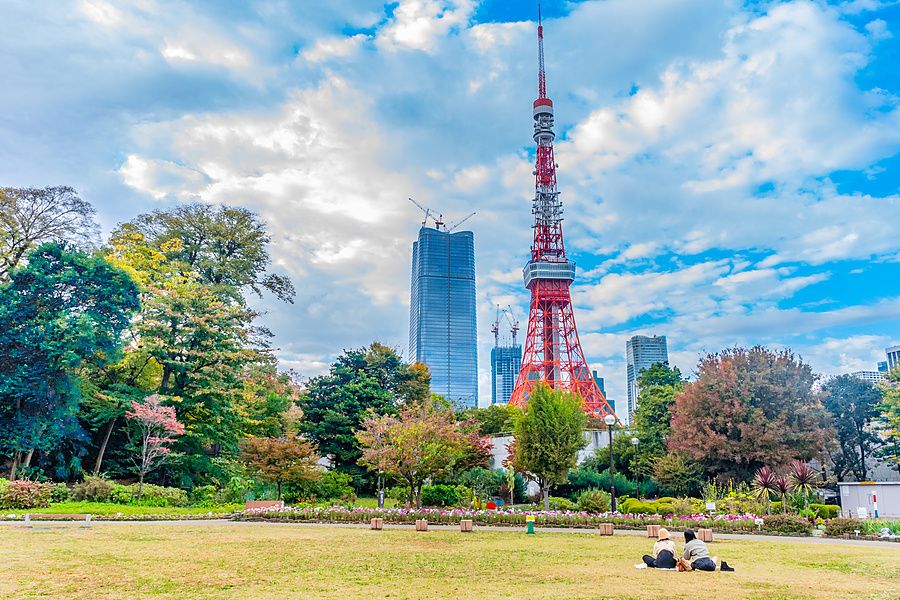 Due persone sedute sul prato dello Shiba Park guardano la Tokyo Tower in una giornata autunnale.