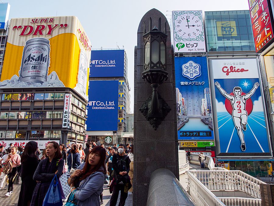 Persone sul ponte Ebisu a Osaka con grandi cartelloni pubblicitari in background.