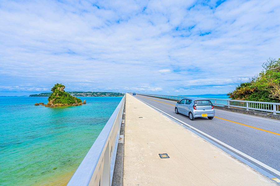 Un'auto percorre il ponte di Kouri a Okinawa, con un isolotto verde in mezzo al mare azzurro.