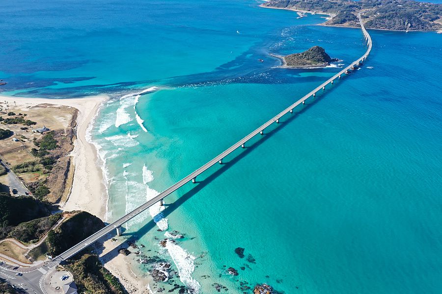 Veduta aerea zenitale del ponte di Tsunoshima che attraversa un mare azzurro cristallino verso un isolotto.