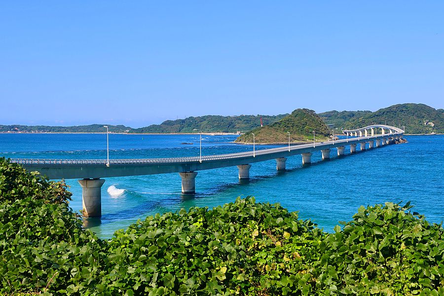 Ponte di Tsunoshima che attraversa il mare blu brillante verso una costa collinosa e verdeggiante in Giappone.