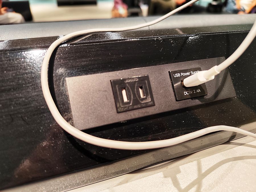 Presa di corrente con porta USB e cavo collegato installata su una struttura nera in un ambiente pubblico.