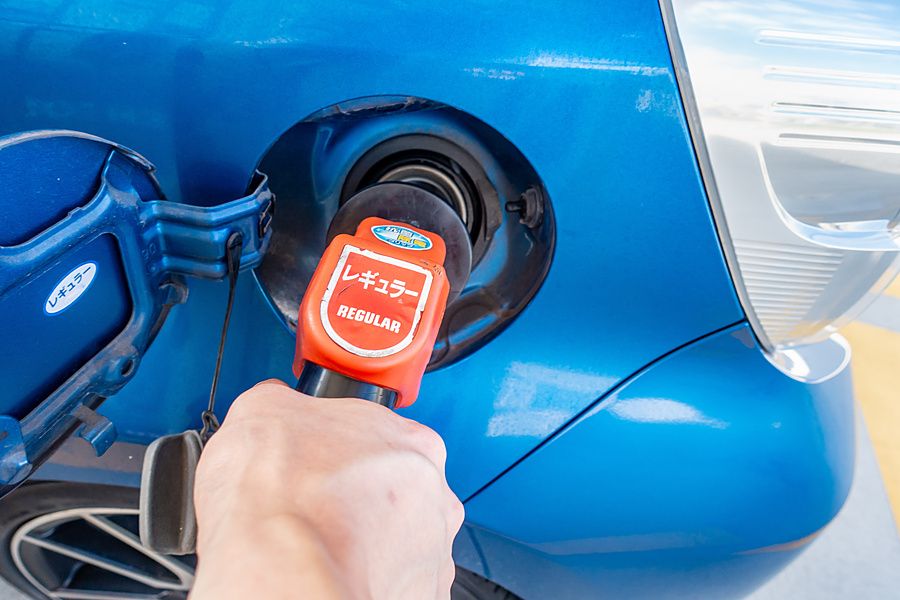 Mano che inserisce l'ugello rosso di una pompa di benzina nel serbatoio di un'auto blu in Giappone.