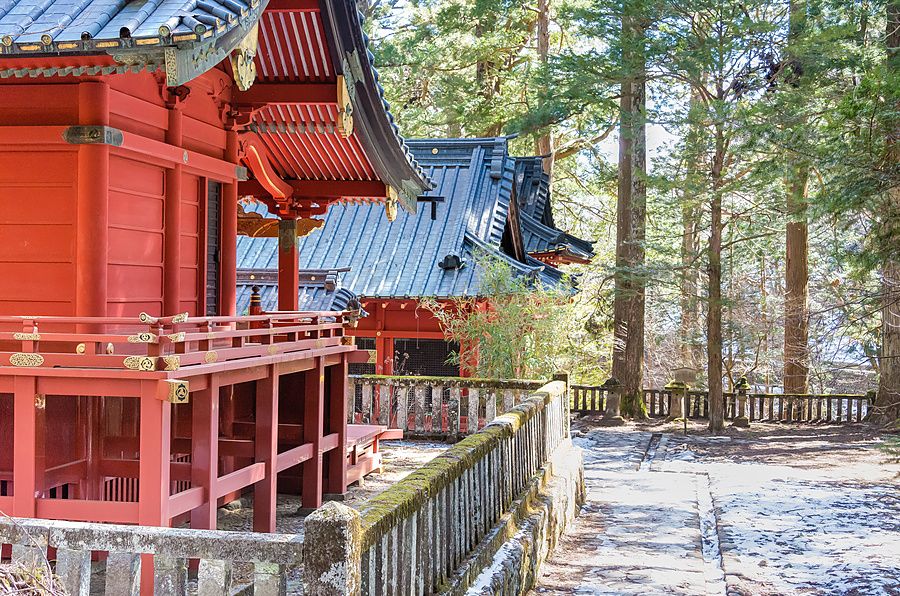 Santuario Takinoo a Nikko con edifici in legno rosso e neve su un sentiero circondato da alti alberi.
