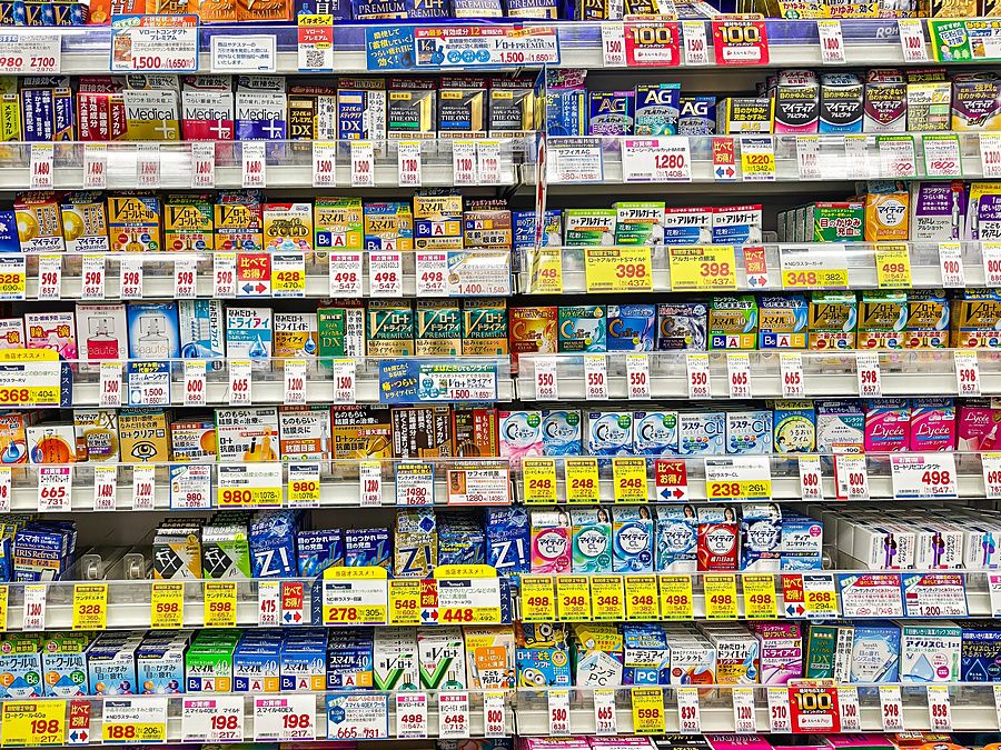 Scaffali di una farmacia ad Akihabara pieni di flaconi di collirio e prodotti sanitari con etichette di prezzo.