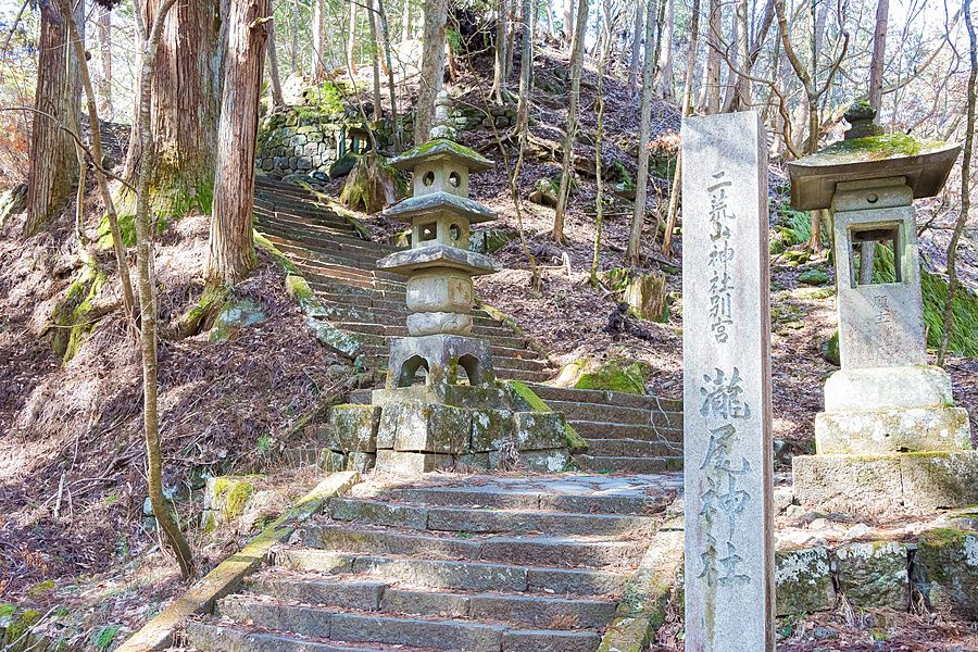 Una antica scalinata in pietra circondata da alberi e lanterne presso il santuario Takinoo a Nikko in Giappone.