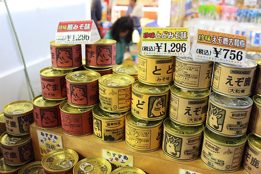 Pile di scatolette di cibo giapponese con illustrazioni di animali su uno scaffale in un negozio.