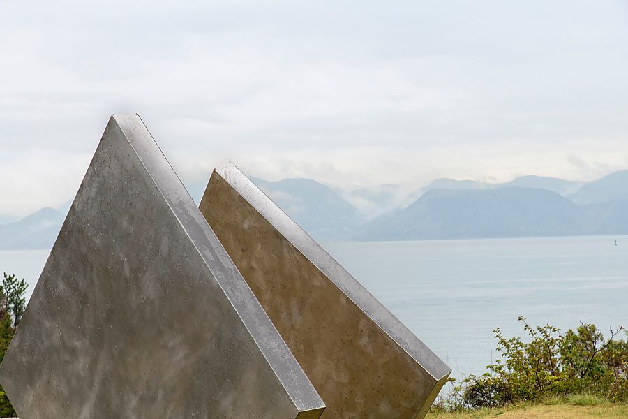 Scultura metallica geometrica davanti al mare e montagne sullo sfondo.