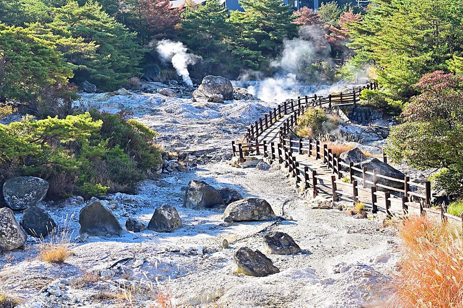 Passerella di legno che attraversa un campo geotermico attivo con vapore e rocce vulcaniche a Unzen Jigoku.