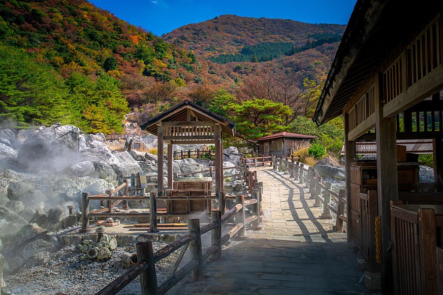 Passerella pedonale in pietra tra rocce vulcaniche fumanti e strutture in legno a Unzen Jigoku in Giappone.