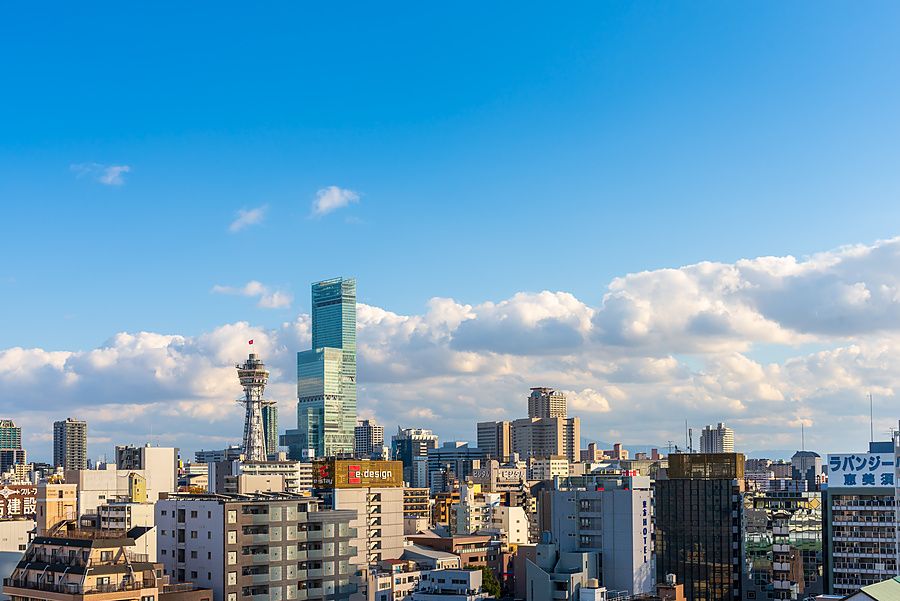 Veduta panoramica degli edifici e grattacieli di Osaka con la Torre Tsutenkaku e l'Abeno Harukas sotto un cielo azzurro.