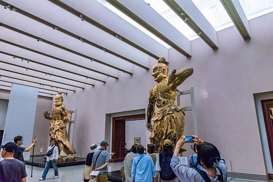 Visitatori osservano due grandi statue dorate dei guardiani Nio esposte al Museo Nazionale di Nara.