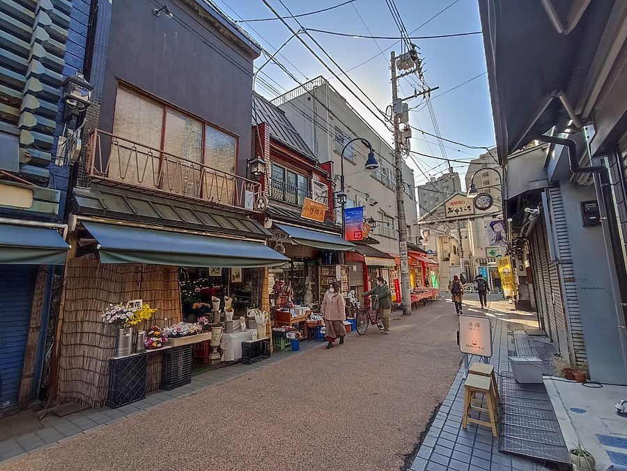 Veduta di una tipica strada storica del quartiere Yanaka a Tokyo con negozi e persone che camminano.