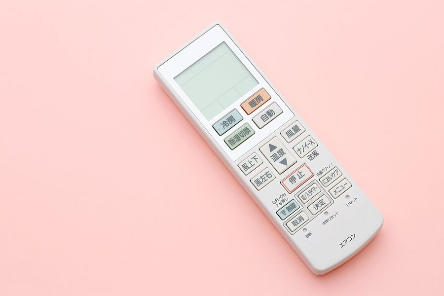 Telecomando per condizionatore d'aria con tasti in giapponese su sfondo rosa pastello.