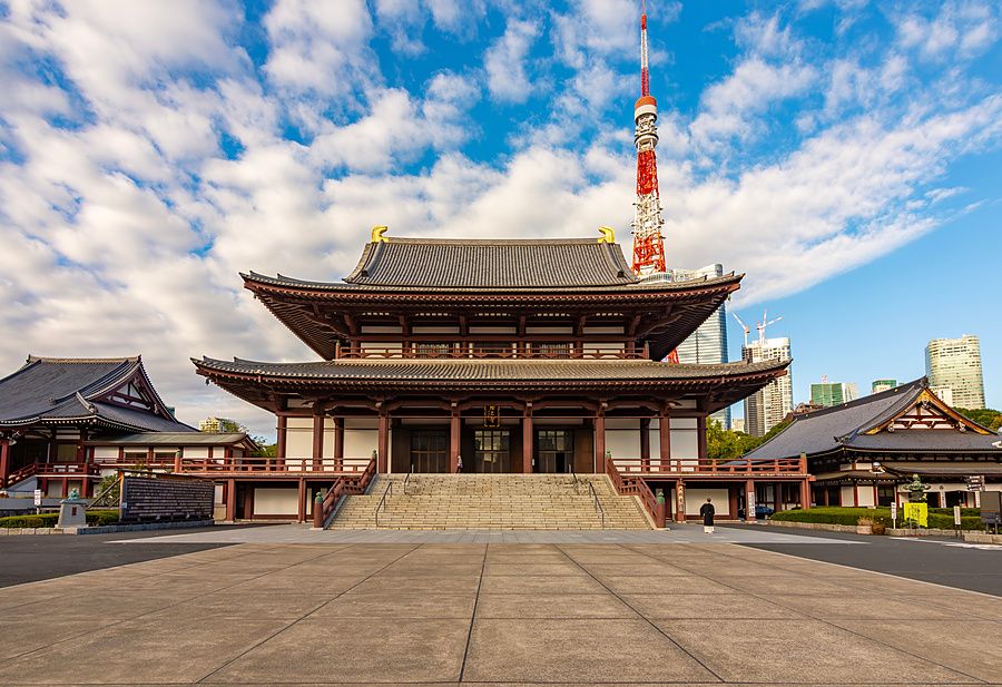 Veduta frontale del tempio Zojo-ji con la Tokyo Tower sullo sfondo sotto un cielo azzurro parzialmente nuvoloso.
