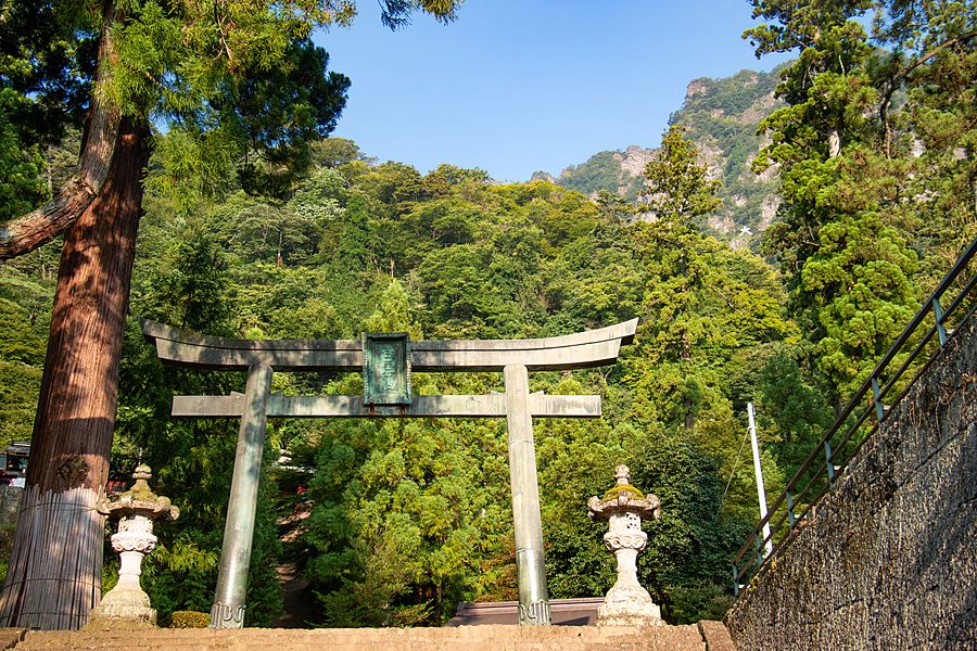 Portale torii in pietra e lanterne in un bosco ai piedi del monte Myogi in Giappone.