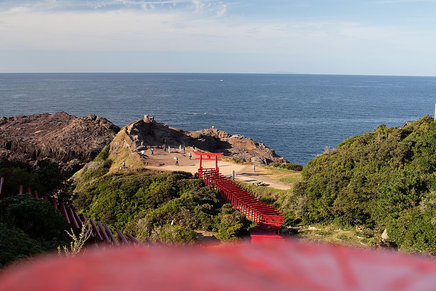 Sentiero con torii rossi che si estende su una scogliera affacciata sul mare in una giornata soleggiata in Giappone.