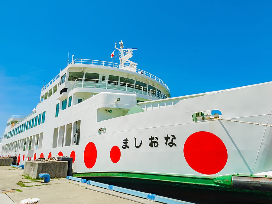 Traghetto bianco decorato con grandi cerchi rossi ormeggiato al molo a Naoshima sotto un cielo blu acceso.
