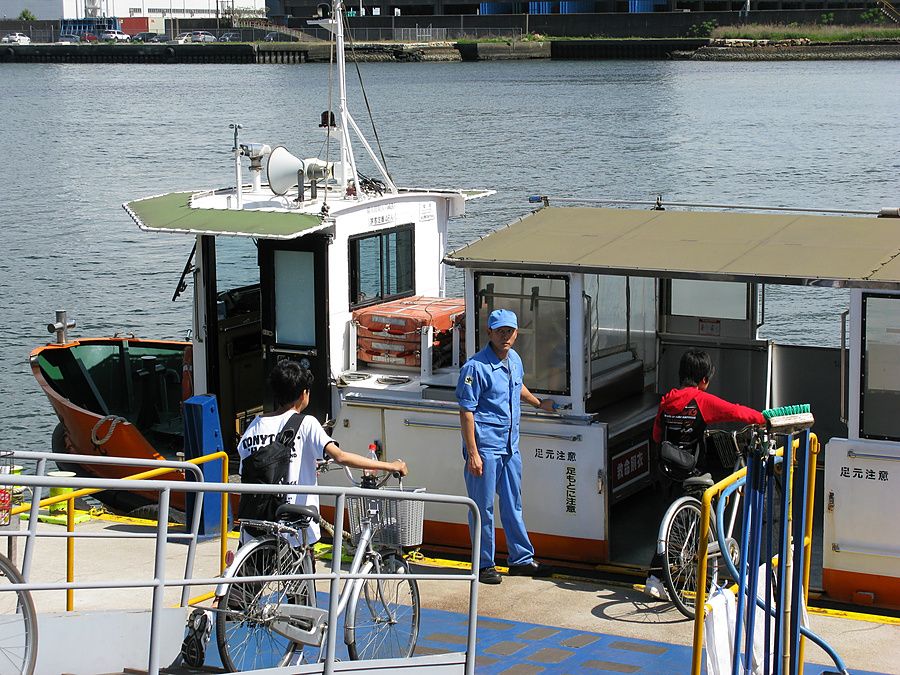 Addetto in divisa blu assiste due persone con bicicletta mentre salgono su un traghetto a Osaka.