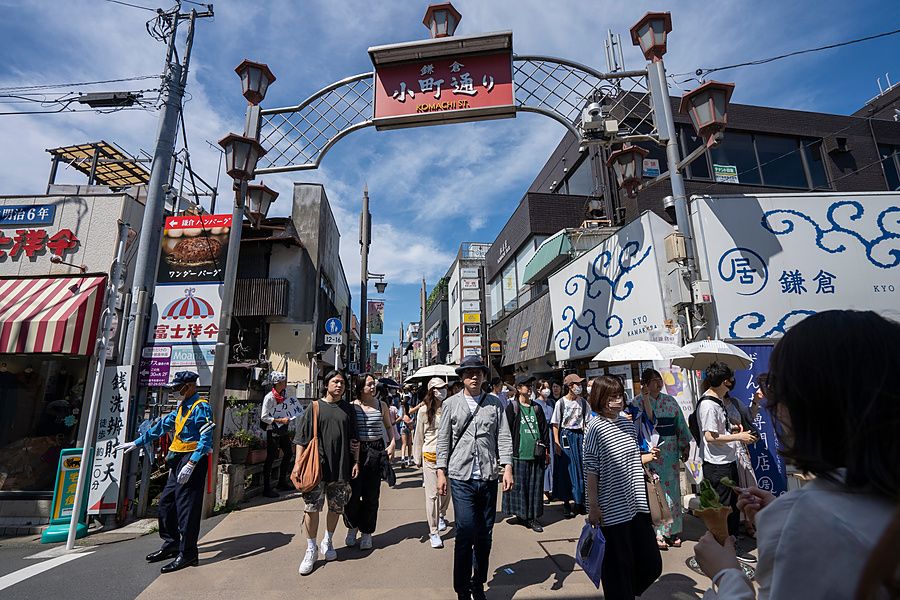 Persone camminano sotto l'arco d'ingresso della via Komachi-dori a Kamakura in una giornata di sole.