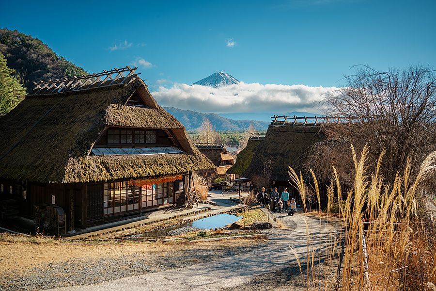 Case tradizionali con tetto di paglia a Saiko Iyashi no Sato Nenba con il monte Fuji sullo sfondo sotto un cielo azzurro.