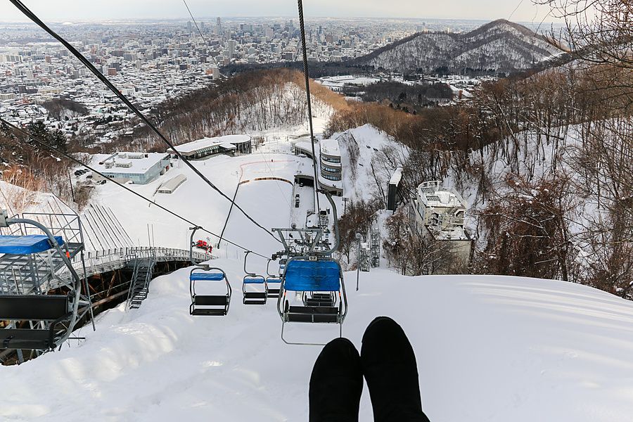 Veduta dall'alto da una seggiovia verso la città di Sapporo innevata e il trampolino olimpico di Okurayama.