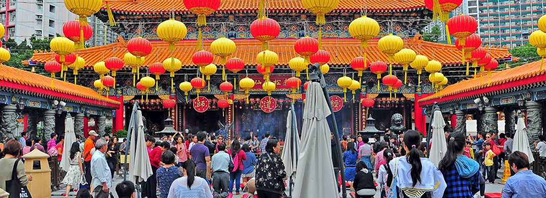 Il tempio di Wong Tai Sin, con lanterne gialle e rosse, e molte persone durante una celebrazione.