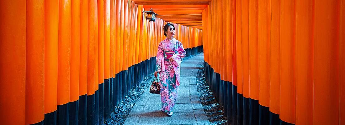 Una donna in kimono cammina tra i portali rossi del Fushimi Inari a Kyoto.