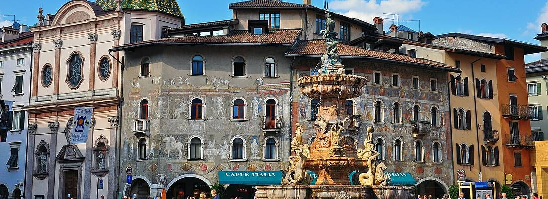 Piazza Duomo a Trento, la fontana in primo piano e dietro dei raffinati affreschi.