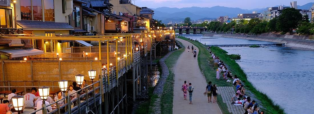 Persone camminano al tramonto sulle rive del fiume Kamogawa a Kyoto.