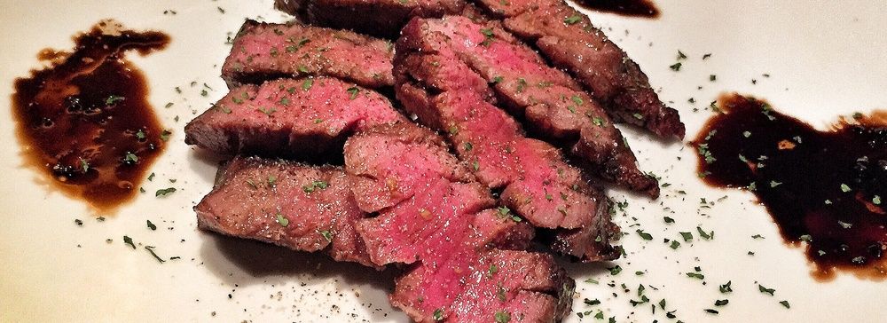 Fette di carne di manzo con erbe e salse su un piatto.