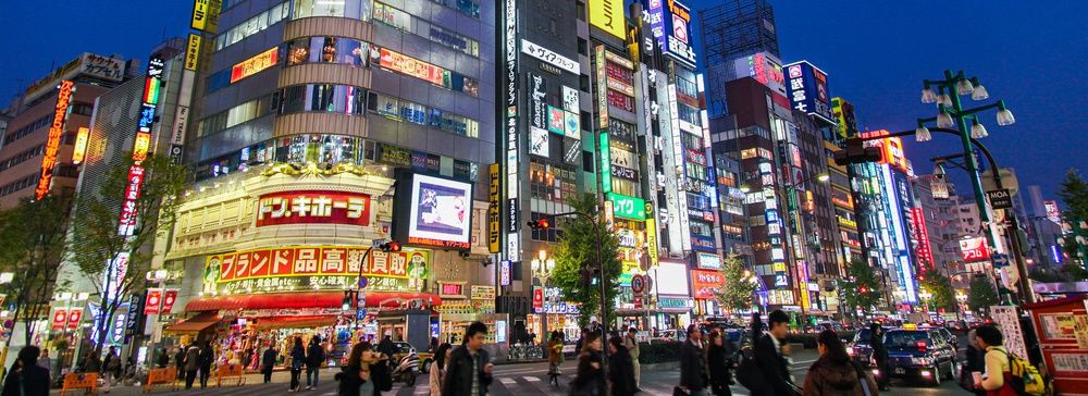 Strada di Shinjuku illuminata da insegne al neon con persone e negozi.