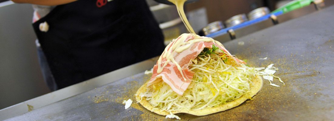 Una cameriera intenta nella preparazione di un okonomiyaki.