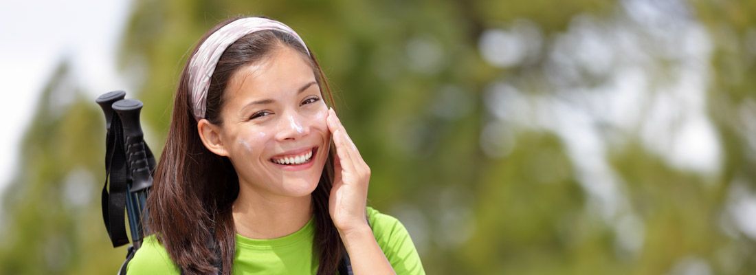 Ragazza che fa trekking e si applica la crema da sole al viso.