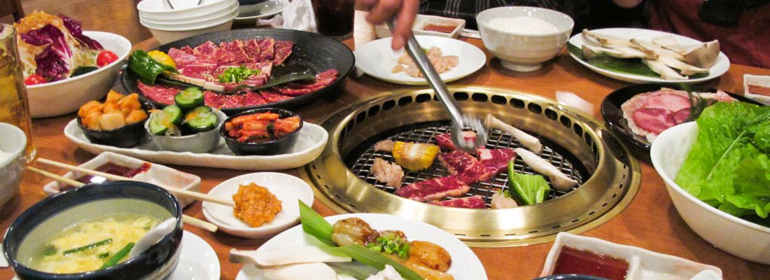 Tavolo imbandito e un commensale che prepara lo yakiniku, carne alla griglia.