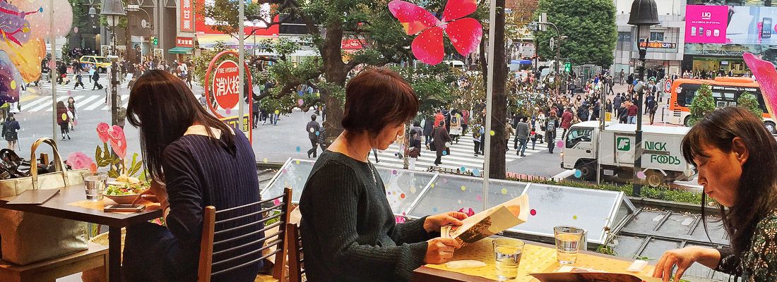 Persone sedute ai tavoli vicino alle finestre all'Occitane Cafe a Shibuya, sullo sfondo il famoso incrocio.