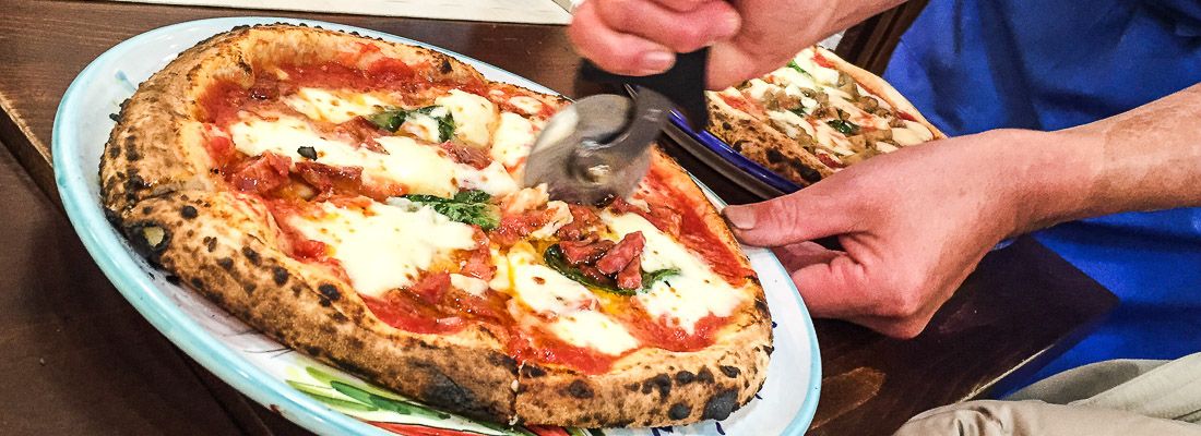 Un cameriere taglia una pizza margherita con un pizza cutter.