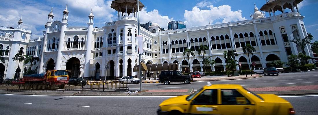 Edificio storico a Kuala Lumpur con taxi giallo in primo piano.