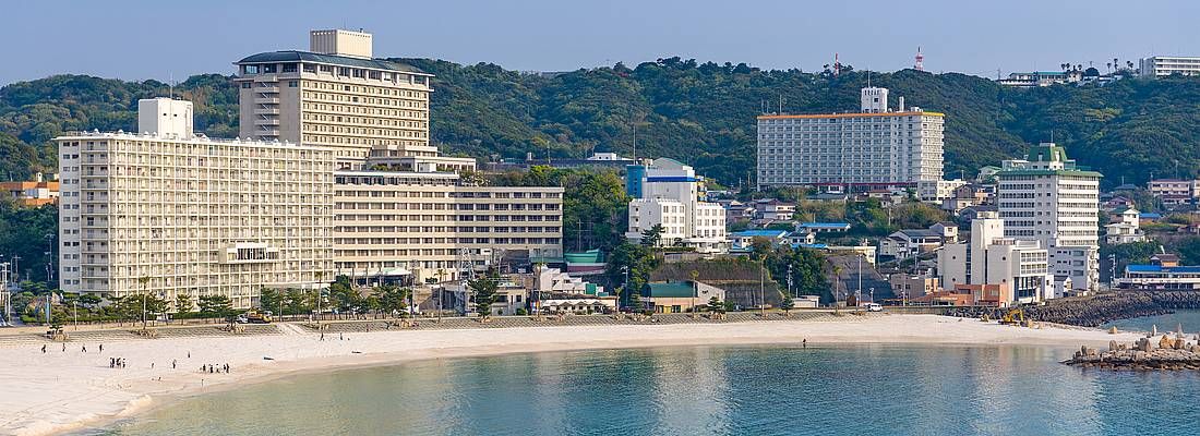 Spiaggia di Shirahama con edifici sulla riva e colline verdi sullo sfondo.