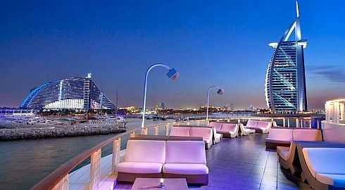 Tavoli in un ristorante all'aperto a dubai, al tramonto, con in lontananza la "vela di Dubai".