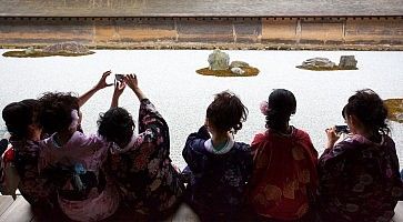 Ragazze in kimono sedute ammirano e fotografano il santuario Ryoanji.