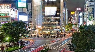 L'incrocio di Shibuya di notte, mentre il traffico sfreccia e le persone attendono di attraversare la strada.
